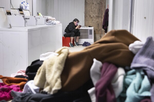 Vera, manager of the Akiachak village wash-a-teria, uses a cell phone while keeping watch over washing machines, Friday, Aug. 18, 2023, in Akiachak, Alaska. (AP Photo/Tom Brenner)