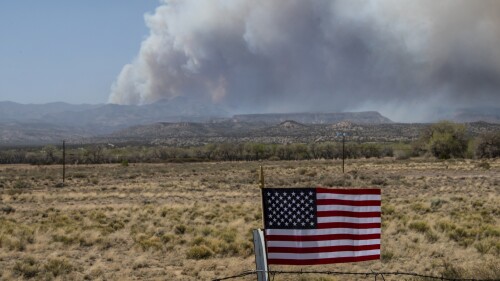 FILE - An American Flag on a fence blows in the wind along NM 22 as the Cerro Pelado Fire burns in the Jemez Mountains, April 29, 2022, in Cochiti, N.M. The U.S. Forest Service said on Monday, July 24, 2023, that its own prescribed burn started the 2022 wildfire that nearly burned into Los Alamos, N.M. (Robert Browman/The Albuquerque Journal via AP, File)