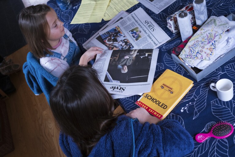 Natalia Bednar, left, looks at a newspaper beside her sister, Valencia, before going to school, Friday, Feb. 2, 2024, in Chevy Chase, Md. (AP Photo/Tom Brenner)