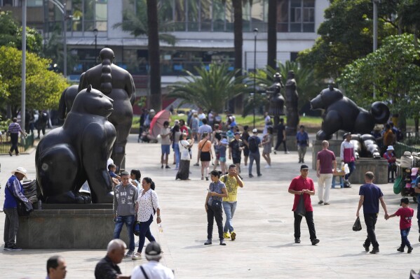 Visitors walk through Botero Plaza in Medellin, Colombia, Thursday, Feb. 1, 2024. Medellin was once the heart of a brutal war involving the Colombian government, drug cartels, and other armed groups, but a sharp dip in violence here has attracted a flood of tourists. (AP Photo/Fernando Vergara)