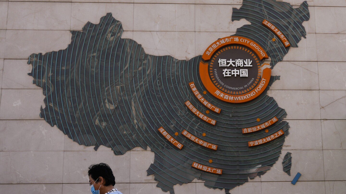 FILE - A woman walks past a map showing Evergrande development projects in China, at an Evergrande city plaza in Beijing on Sept. 21, 2021. Police in 