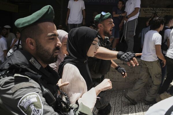 Israeli police officers escort Palestinian women past Israelis celebrating Jerusalem Day, an Israeli holiday celebrating the capture of east Jerusalem in the 1967 Mideast war, in Jerusalem's Old City, Monday, May 26, 2025. (AP Photo/Leo Correa)