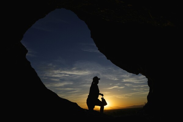 FILE - A hiker walks past the Hole-in-the-Rock at Papago Park during sunrise July 17, 2023, in Phoenix. Scientists say by far the biggest cause of the recent extreme warming is human-caused climate change and a natural El Nino. But some say there’s got to be something more. (AP Photo/Ross D. Franklin, File)