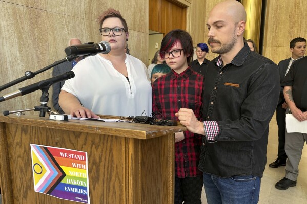 Parents Devon and Robert Dolney, of Fargo, stand with their 12-year-old child, Tate, center, during a press conference, Thursday, Sept. 14, 2023,, at the state Capitol in Bismarck, N.D. Tate Dolney is a transgender boy and a plaintiff in a lawsuit to block North Dakota's ban on gender-affirming care for minors. The law passed North Dakota's Republican-controlled Legislature overwhelmingly earlier this year. Republican Gov. Doug Burgum signed the bill into law in April. A Gender Justice sign on the press conference lectern reads "We stand with North Dakota families." (AP Photo/Jack Dura)