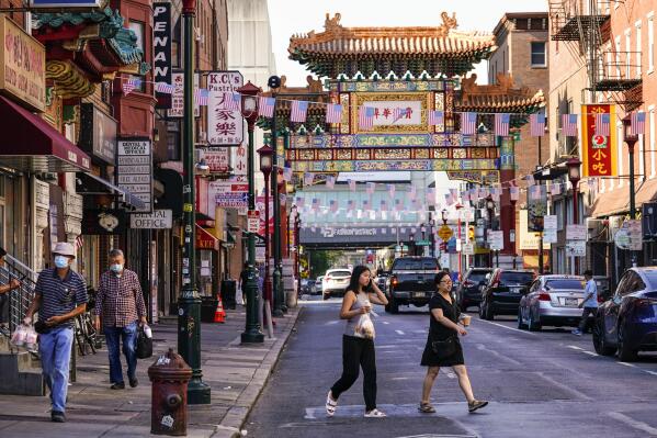 Pedestrians cross 10th Street in the Chinatown neighborhood of Philadelphia, Friday, July 22, 2022. Organizers and members of Philadelphia's Chinatown say they were surprised by the 76ers' announcement that they hope to build a $1.3 billion arena just a block from the community’s gateway arch. (AP Photo/Matt Rourke)