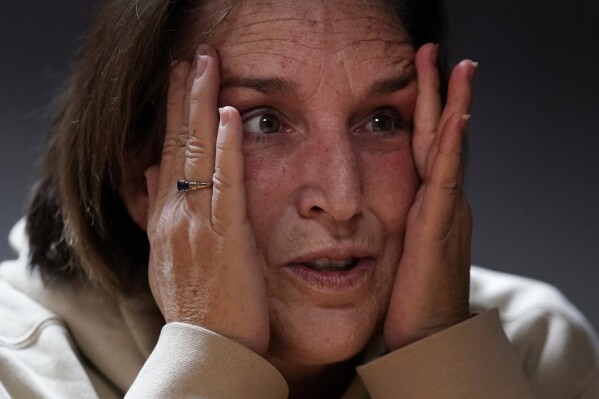 Shooting survivor Tammy Asselin clutches her face while reflecting on surviving a mass shooting by Army reservist Robert Card, during an interview, Wednesday, Dec. 27, 2023, in Lewiston, Maine. (AP Photo/Charles Krupa)