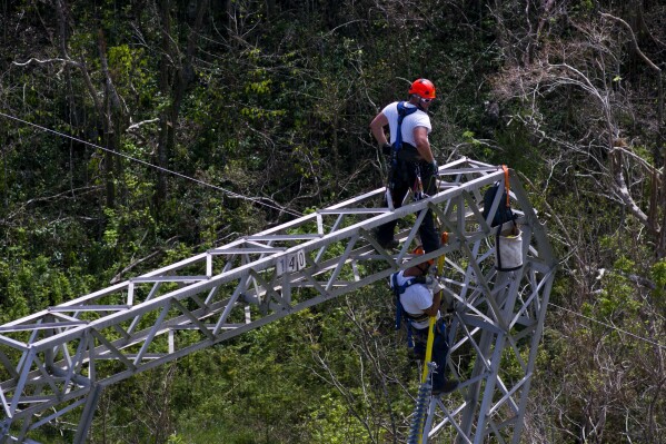 FILE - Workers restore power lines damaged by Hurricane Maria in Barceloneta, Puerto Rico, Oct. 15, 2017. Activists and environmental groups including the Sierra Club are suing on Monday, Aug. 14, 2023, Puerto Rico’s government over the planned location of dozens of renewable energy projects meant to ease the U.S. territory’s power woes. (AP Photo/Ramon Espinosa, File)