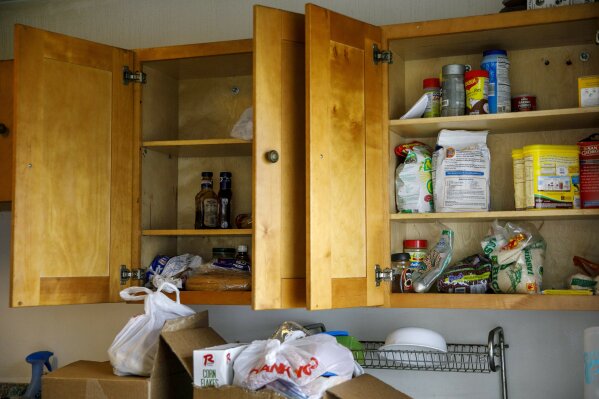 Arely's kitchen cabinets are down to a few items including flour, dried beans, rice, and barbecue sauce, Tuesday, April 14, 2020, in Baltimore. She is a recent asylum seeker from Honduras who says and her children are fleeing gang violence. On the counter are two boxes of food that her sister Janeth's family brought to them after scouring Washington food banks and churches to get enough food for the families to share. The previous week one chicken was cut up into portions and each of the family of five was able to eat one meal a day. "We have to set limits on meals," says Arely, "we have no choice." (AP Photo/Jacquelyn Martin)