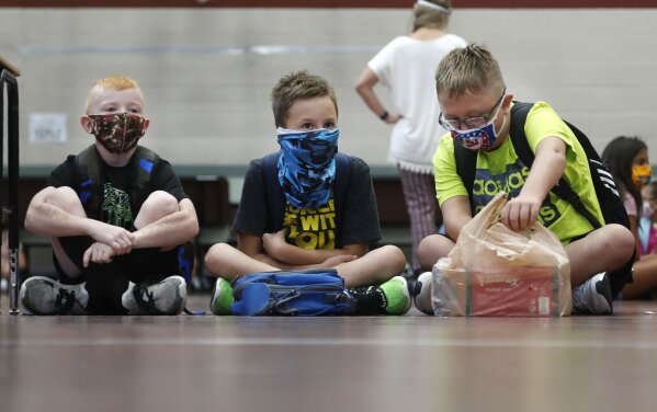FILE - In this Aug. 5, 2020, file photo, wearing masks to prevent the spread of COVID19, elementary school students wait for classes to begin in Godley, Texas. As schools reopen around the country, their ability to quickly identify and contain coronavirus outbreaks before they get out of hand is about to be put to the test. (AP Photo/LM Otero, File)