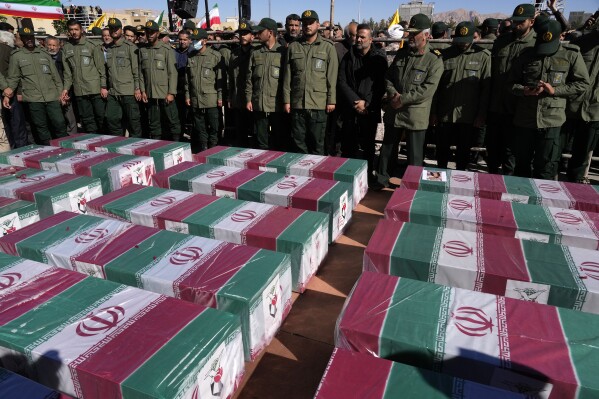 Revolutionary Guard members stand over the flag-draped coffins of victims of Wednesday's bomb explosion during their funeral ceremony in the city of Kerman about 510 miles (820 kms) southeast of the capital Tehran, Iran, Friday, Jan. 5, 2024. Iran on Friday mourned those slain in an Islamic State group-claimed suicide bombing targeting a commemoration for a general slain in a U.S. drone strike in 2020. (AP Photo/Vahid Salemi)