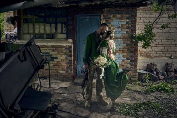 Volunteer military medics, code names Nikita and Polka, wearing national clothes, share a kiss during their wedding ceremony at their position on the frontline in the Donetsk region, Ukraine, Thursday, June 29, 2023. (AP Photo/Libkos)