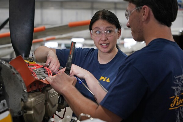 File - Students at the Pittsburgh Institute of Aeronautics Nikki Reed, center, and William Onderdork study the engine on an Cessna 310 aircraft in West Mifflin, Pa., May 2, 2023. On Friday, the U.S. government issues its latest monthly jobs report. (AP Photo/Gene J. Puskar, File)