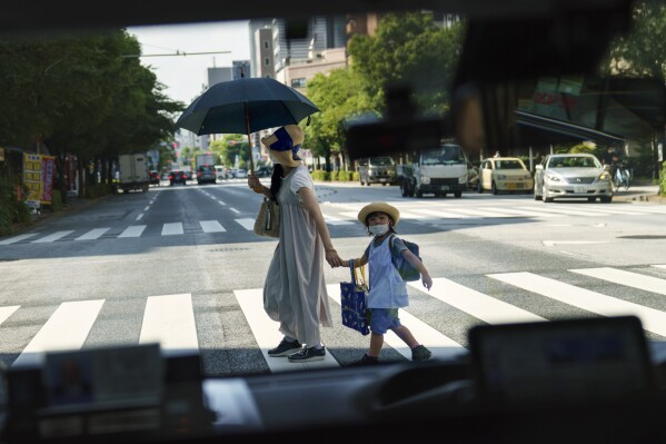 FILE - A pedestrian crossing a street with a child is seen through a taxi window in Tokyo, Monday, July 19, 2021. Japan’s birth rate fell to a new low for the eight straight year in 2023, according to Health Ministry data released on Wednesday, June 5, 2024. (AP Photo/David Goldman, File)