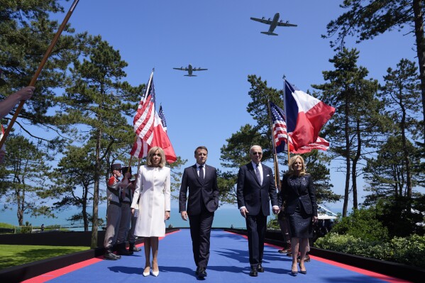 2024年6月6日，星期四，在诺曼底举行的诺曼底登陆80周年纪念仪式上，乔·拜登总统、第一夫人吉尔·拜登、法国总统埃马纽埃尔·马克龙和他的妻子布丽姬·马克龙走在舞台上。（美联社照片/埃文·武奇）