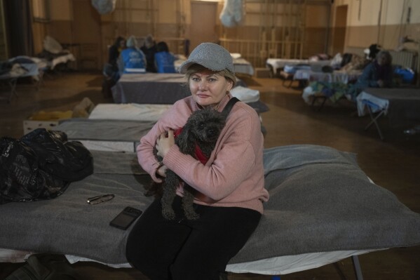 Iryna Prohoda, a refugee from Pokrovsk, holds her dog as she sits on a bed in a city theatre that hosts refugees running from Russian offensive in the Donetsk region, in Pavlohrad, Dnipropetrovsk region, Ukraine, Thursday, Dec. 12, 2024.(AP Photo/Efrem Lukatsky)