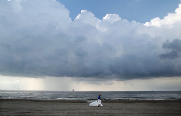 FILE - A worker leaves the beach as storm clouds approach in Grand Isle, La., May 30, 2010. When a deadly explosion destroyed BP's Deepwater Horizon drilling rig in the Gulf of Mexico, tens of thousands of ordinary people were hired to help clean up the environmental devastation. These workers were exposed to crude oil and the chemical dispersant Corexit while picking up tar balls along the shoreline, laying booms from fishing boats to soak up slicks and rescuing oil-covered birds. (AP Photo/Jae C. Hong, File)