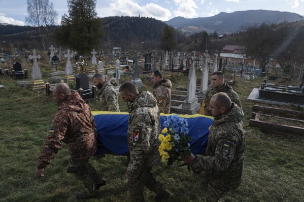 Ukrainian servicemen carry the coffin of their comrade Vasyl Boichuk who was killed in Mykolayiv in March 2022, during his funeral ceremony at the cemetery in Iltsi village, Ukraine, Tuesday, Dec. 26, 2023. (AP Photo/Evgeniy Maloletka)
