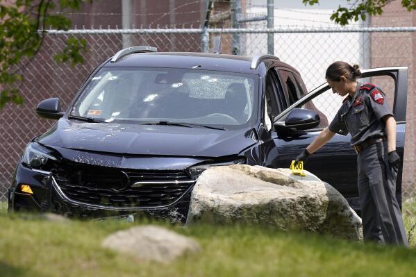 A Rhode Island state trooper places an evidence marker near a vehicle with holes in the windshield, Wednesday, May 24, 2023, at the scene of a crash, in Cranston, R.I. A suspect shot and killed two people and wounded a third in Rhode Island, before fleeing the scene and being shot and killed by police, authorities said. (AP Photo/Steven Senne)