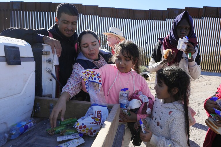 Gerston Miranda, left, and his family from Ecuador get food and water before joining hundreds of migrants gathering along the border Tuesday, Dec. 5, 2023, in Lukeville, Ariz. (AP Photo/Ross D. Franklin)
