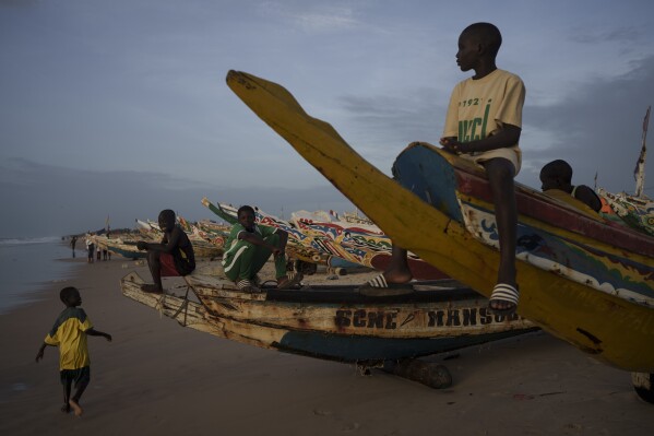 Niños sentados en piraguas, embarcaciones senegalesas utilizadas por pescadores e inmigrantes, en la playa de Fass Boye, Senegal, el martes 29 de agosto de 2023. (AP Foto /Felipe Dana)