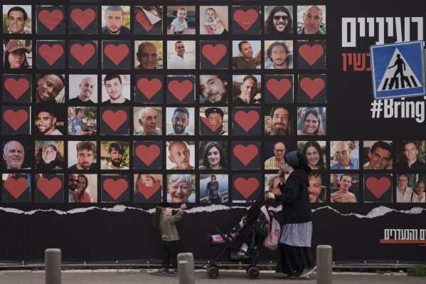 FILE - A woman and her children walk past a wall with photographs of hostages who were kidnapped during the Oct. 7 Hamas cross-border attack in Israel in Jerusalem, Monday, Feb. 26, 2024. (AP Photo/Leo Correa, File)