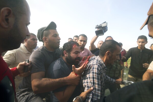 Palestinezët transportojnë një civil izraelit të kapur, në qendër, nga Kibbutz Kfar Azza në Rripin e Gazës të shtunën, 7 tetor 2023. Sundimtarët militantë të Hamasit të Rripit të Gazës kryen një sulm të paprecedentë, me shumë fronte mbi Izraelin në agim të së shtunës, duke qëlluar mijëra raketa ndërsa dhjetëra luftëtarë të Hamasit depërtuan në kufirin fort të fortifikuar në disa vende nga ajri, toka dhe deti dhe duke e zënë vendin jashtë roje në një festë të madhe. (AP Photo/Hatem Ali)