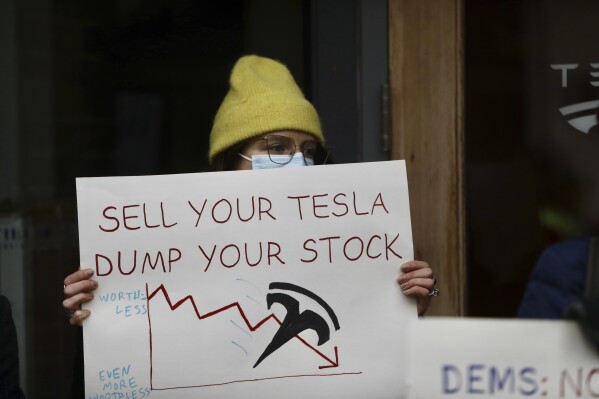 A person protesting Elon Musk's actions in the Trump administration holds a sign outside a Tesla showroom in Seattle on Thursday, Feb. 13, 2025. (AP Photo/Manuel Valdes, File)