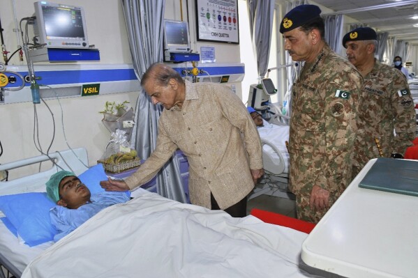 In this photo released by the Prime Minister Office, Prime Minister Shehbaz Sharif, center, checks on a child injured in the suicide bombing in Khuzdar, as Army Chief Field Marshal Asim Munir, second right, looks on during their visit to a hospital in Quetta, Pakistan, Wednesday, May 21, 2025. (Prime Minister Office via AP)
