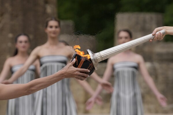 FILE - Actress Mary Mina, playing high priestess, right, lights a torch during the official ceremony of the flame lighting for the Paris Olympics, at the Ancient Olympia site, Greece, April 16, 2024. The Olympic torch finally enters France when it reaches the southern seaport of Marseille on Wednesday May 8, 2024, on an armada from Greece. After leaving Marseille a vast relay route will be undertaken before the torch's odyssey ends on July 27 in Paris. (AP Photo/Thanassis Stavrakis, File)