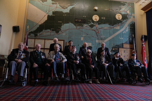 Normandy campaign veterans pose in the 'Map Room' which shows the large diagram of the D-Day invasion plans, at Southwick army base near Portsmouth, England, Monday, June 3, 2024. The map was used by Naval planners under the command of of British Admiral Bertram Ramsay. (AP Photo/Alastair Grant)