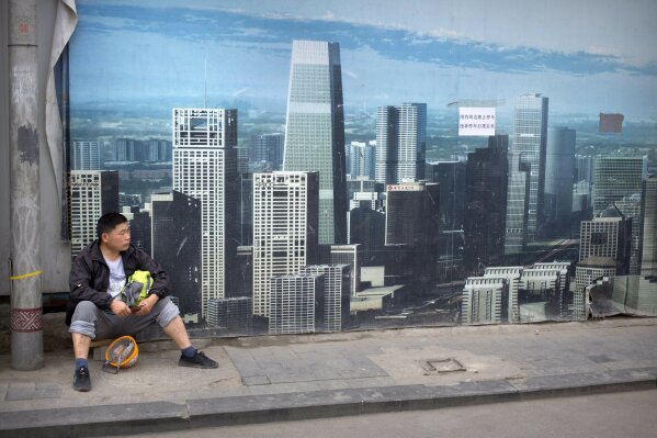 FILE - In this May 16, 2019, file photo, a worker sits in front of a billboard at a construction site in Beijing. Thirty years since the Tiananmen Square protests, China's economy has catapulted up the world rankings, yet political repression is harsher than ever. (AP Photo/Mark Schiefelbein, File)