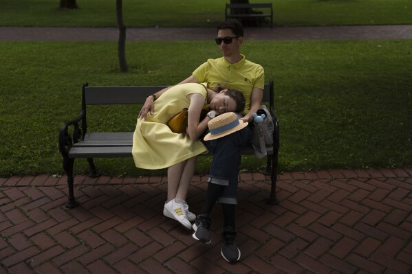 FILE - A woman takes a nap on the lap of her husband on a bench at Saint Sophia Cathedral in Kyiv, Ukraine, Sunday, July 30, 2023. Life in the capital of a war-torn country seems normal on the surface. In the mornings, people rush to their work holding cups of coffee. Streets are filled with cars, and in the evenings restaurants are packed. But the details tell another story. (AP Photo/Jae C. Hong, File)