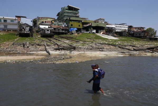 FILE - Uanderson Marinho de Souza, 40, carries his son to school across the much-diminished Negro River, amid an ongoing drought in Manaus, Brazil, Sept. 26, 2023. The extreme drought sweeping across Brazil’s Amazon rainforest is already impacting hundreds of thousands of people and killing local wildlife. (AP Photo/Edmar Barros, File)