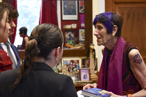 This photo provided by the Office of Congresswoman Rosa DeLauro shows Connecticut U.S. Rep. Rosa DeLauro, right, donning a tattoo, as she talks with interns, Friday, July 28, 2023, in Washington. DeLauro has stood out for years with her colorful clothing and hairstyle, but it took one of her six grandchildren to finally convince the 80-year-old lawmaker to complement her fashion-forward look with a tattoo. (Daniel Robillard/Office of Congresswoman Rosa DeLauro via AP)