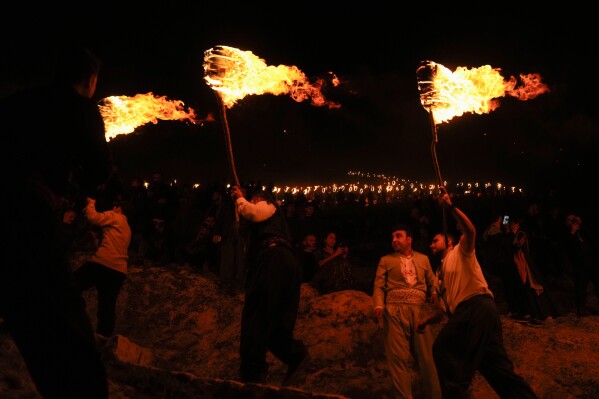 Iraqi Kurds holding lit torches walk up a mountain during a procession to celebrate their Nowruz, the Persian New Year, in Akra, Iraq, Thursday, March 20, 2025. (AP Photo/Hadi Mizban)