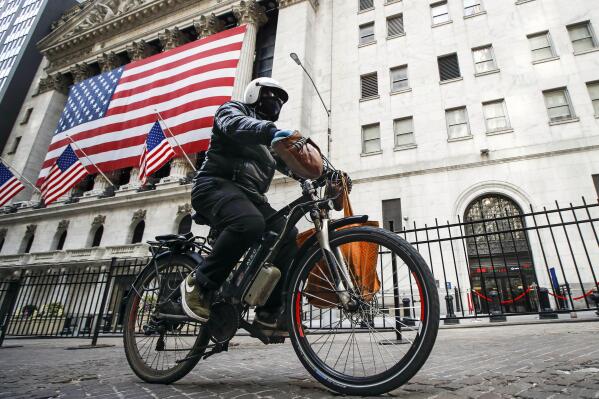 FILE - A delivery worker rides his electric bicycle past the New York Stock Exchange, March 16, 2020, in New York.Lithium ion batteries used to power electric bicycles and scooters have already sparked 22 fires that caused 36 injuries and two deaths in New York City this year, four times the number of fires linked to the batteries by this time last year, city officials said Friday, Feb. 24, 2023. (AP Photo/John Minchillo, File)