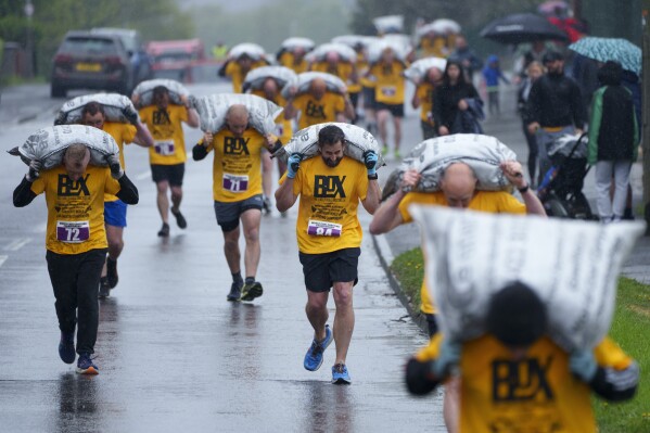 Contestants in the men's veterans race make for the finish carrying 50kg sacks of coal at the World Coal Carrying Championships in Ossett, West Yorkshire, England, Monday, April 21, 2025. (AP Photo/Jon Super)