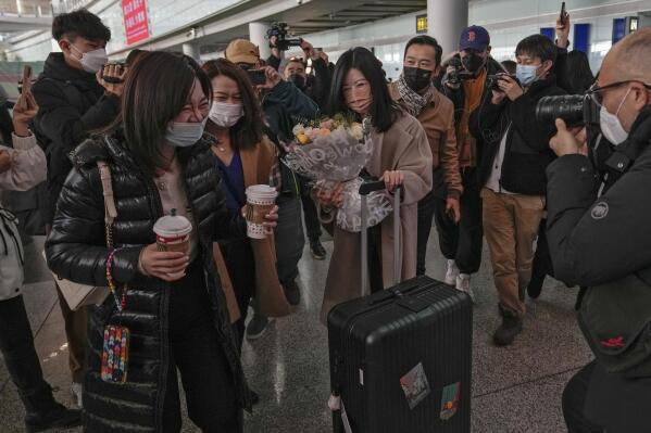 A woman holding a bouquet of flowers reacts with her relatives surrounded by journalists as she arrives from Hong Kong, at Terminal 3 international arrival hall of the Beijing Capital International Airport in Beijing, Sunday, Jan. 8, 2023. Travelers crossing between Hong Kong and mainland China, however, are still required to show a negative COVID-19 test taken within the last 48 hours, a measure China has protested when imposed by other countries. (AP Photo/Andy Wong)
