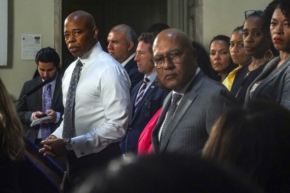 New York Mayor Eric Adams, left, and city officials listen to a reporter's question during a City Hall press conference, Wednesday Aug. 9, 2023, in New York. Adams is calling on the federal government to declare a national emergency to ease the financial crisis the city is facing as it struggles to accommodate thousands of arriving migrants. (AP Photo/Bebeto Matthews)