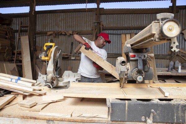 Ex-migrant Eduardo Jimenez saws wood in a carpentry workshop in Cajola, Guatemala, Nov. 29, 2021. Jimenez’s project creates doors and woodwork for homes paid for with money sent home from the U.S. (AP Photo/Megan Janetsky)