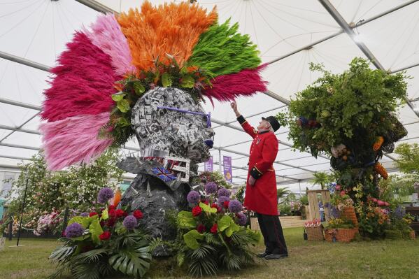 Chelsea Pensioner Peter Wilson reaches up to touch a Punks head with a mohawk created with pampas grass, tropical blooms and preserved leaves part of Chelsea in Bloom by Ricky Paul Flowers at the RHS Chelsea Flower Show in London, Monday, May 19, 2025. (AP Photo/Kirsty Wigglesworth)