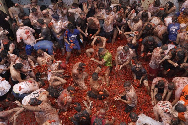 Revellers throw tomatoes at each other during the annual "Tomatina" tomato fight fiesta, in the village of Bunol near Valencia, Spain, Wednesday, Aug. 30, 2023. Thousands gather in this eastern Spanish town for the annual street tomato battle that leaves the streets and participants drenched in red pulp from 120,000 kilos of tomatoes. (AP Photo/Alberto Saiz)