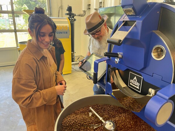 Timothy Styczynski, Head Roaster, UC Davis Coffee Center shows UC Davis Graduating Student Kiara DeGroen, an industrial coffee bean roaster at the Coffee Center at UC Davis in Davis, Calif. on Monday, June 17, 2024. The center which opened last month, is believed to be the first coffee-only research facility opened on any college campus in the U.S. (AP Photo/Haven Daley)