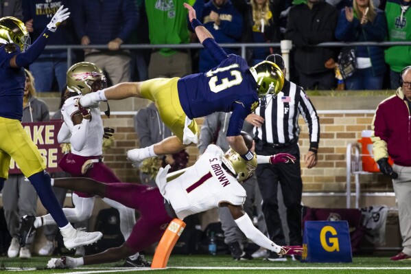 Notre Dame quarterback Riley Leonard (13) jumps into the end zone over Florida State defensive back Shyheim Brown (1) as defensive back Kevin Knowles II (3) also defends during an NCAA college football game Saturday, Nov. 9, 2024, in South Bend, Ind. (AP Photo/Michael Caterina)