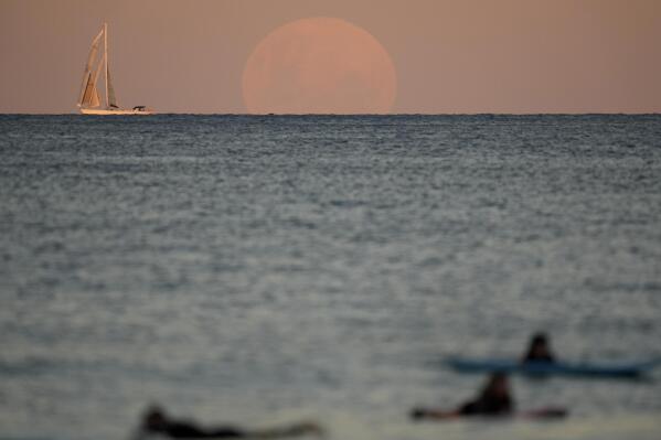 A yacht sails past as the moon rises in Sydney Wednesday, May 26, 2021. A total lunar eclipse, also known as a Super Blood Moon will take place later tonight as the moon appears slightly reddish-orange in color. (AP Photo/Mark Baker)