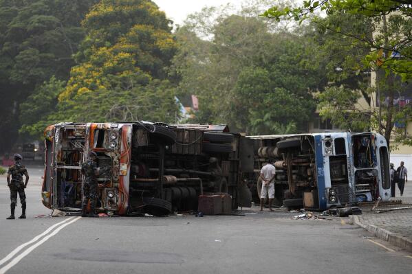 Sri Lankan soldiers stand guard next to burnt buses a day after clashes between government supporters and anti-government protesters in Colombo, Sri Lanka, Tuesday, May 10, 2022. Defying a nationwide curfew in Sri Lanka, several hundred protesters continued to chant slogans against the government Tuesday, a day after violent clashes saw the resignation of the prime minister who is blamed, along with his brother, the president, for leading the country into its worst economic crisis in decades. (AP Photo/Eranga Jayawardena)