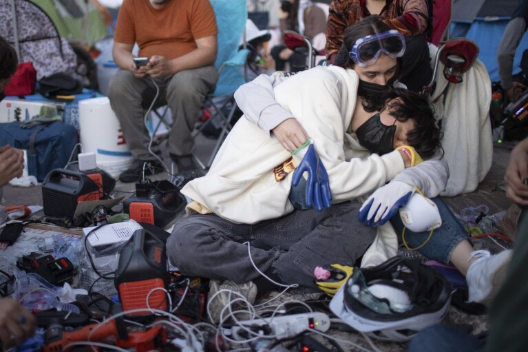 Pro-Palestinian protesters embrace while charging their devices at an encampment on the UCLA campus on Wednesday, May 1, 2024 in Los Angeles.  (AP Photo/Ethan Swope)