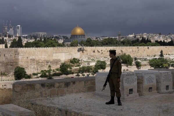 FILE - An Israeli soldier pauses in the Mount of Olives cemetery, just outside of the Old City of Jerusalem, as he turns towards the Dome of the Rock Mosque in the Al-Aqsa Mosque compound, Monday, May 13, 2024. Thousands of mostly ultranationalist Israelis were expected to take part in an annual march through dense Palestinian neighborhoods of Jerusalem's Old City on Wednesday, June 5, in an event that often sees racist chants and brawls. (AP Photo/Maya Alleruzzo, File)