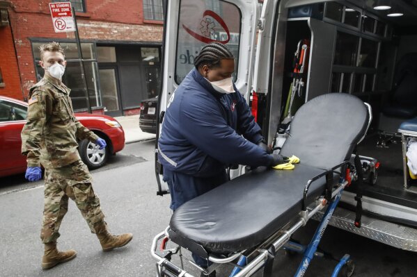 An emergency medical worker cleans his gurney at his ambulance as a member of the National Guard arrives outside Cobble Hill Health Center, Friday, April 17, 2020, in the Brooklyn borough of New York. The despair wrought on nursing homes by the coronavirus was laid bare Friday in a state survey identifying numerous New York facilities where multiple patients have died. Nineteen of the state's nursing homes have each had multiple deaths linked to the pandemic. (AP Photo/John Minchillo)