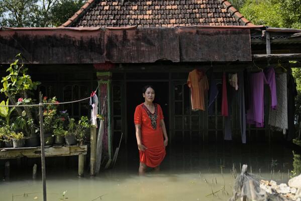 Zuriah stands outside her flooded home in Mondoliko, Central Java, Indonesia, Monday, Aug. 1, 2022. Unable to afford to move to a new home, Zuriah continues to live in the house even as nearly all of her neighbors move away. (AP Photo/Dita Alangkara)